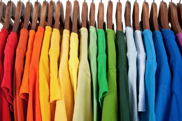 A Row Of Colourful T Shirts Organized By Colour On Wooden Hangers.