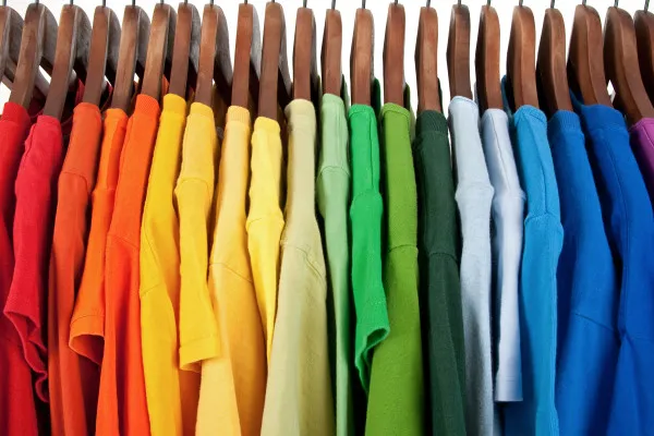 A Row Of Colourful T Shirts Organized By Colour On Wooden Hangers.